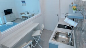 Una cocina compacta con un lavamanos, un pequeño comedor y una ventana con vista al salón.