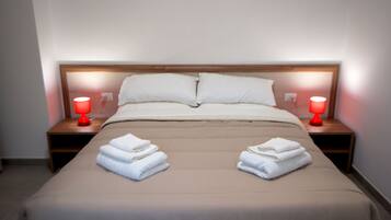 A neatly made bed with two pillows, two red bedside lamps, and folded towels on each side.