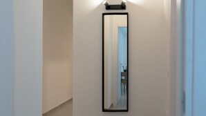Un pasillo con un espejo grande en la pared, una puerta a la derecha y una lámpara sobre el espejo.