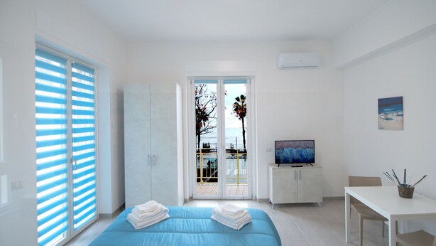 Un dormitorio moderno con una cama, un televisor y un balcón con vistas al mar.