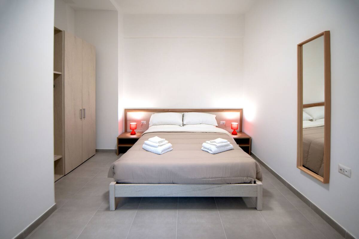A neatly arranged bedroom with a bed, bedside tables, and a wardrobe.