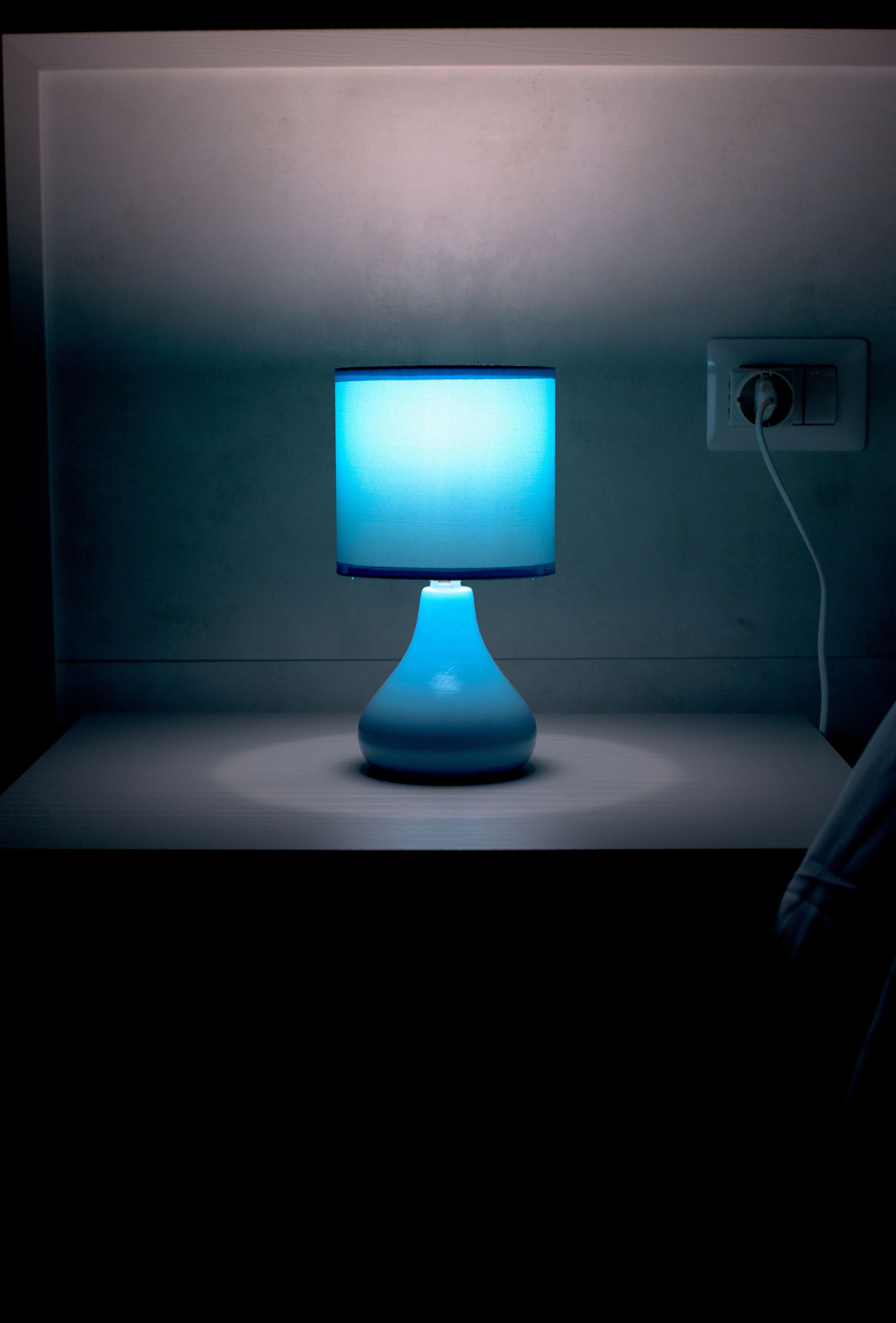 Een nachtkastje met een blauwe lamp en een computerscherm.