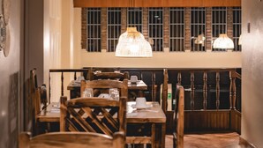 A restaurant interior with wooden tables and chairs, hanging pendant lights, and a view of the street through large windows. - HOTEL EL MORLACO  (Cuenca)