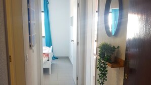 A hallway with a tiled floor, a bed with a blue curtain, and a potted plant on a shelf. - Chabella - Charm Beach Lofts & Apartments - Centeanes (Carvoeiro)
