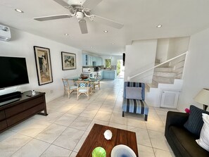 Un salon moderne avec un téléviseur à écran plat, une table à manger et des chaises, un escalier et une cuisine en arrière-plan.