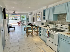 A modern kitchen with light blue cabinets, a dining area with wooden chairs, and a view through the glass door to the outside.