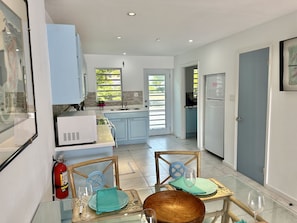 A modern kitchen with light blue cabinets, a white refrigerator, and a dining area with two chairs and a table set for two. - The Salty Palm Villa (Jolly Harbour)