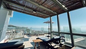 Een terras op het dak met ligbedden, een tafel en uitzicht op de oceaan.