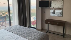 Een hotelkamer met een groot bed, een aan de muur bevestigde televisie, een nachtkastje en uitzicht op de stad door het raam.