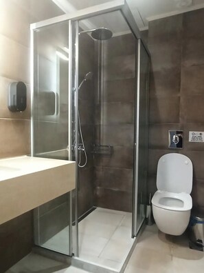 A modern bathroom with a glass-enclosed shower, a white toilet, and a sink with a soap dispenser. - King Crimson Luxury Apartments (Platanias)