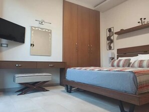 A bedroom with a bed, a wardrobe, a desk, and a television. - King Crimson Luxury Apartments (Platanias)