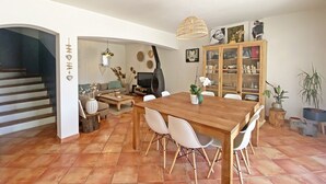 Een ruime woonkamer met een houten eettafel, witte stoelen, een televisie en een boekenkast.