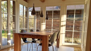 A dining area with a wooden table and chairs, large windows, and a view of the outdoors. - "storchenhuus", Wunderschönes Fachwerkhaus , Garten , 200 m vom Bodden (Wiek)