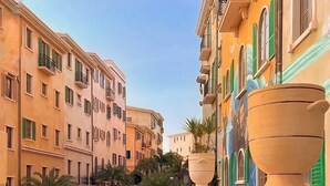 Un couple se tient sur un balcon donnant sur une rue bordée d’immeubles et de palmiers.