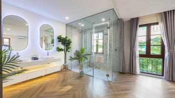 A modern bathroom with a glass shower enclosure, a large mirror, and a wooden floor.