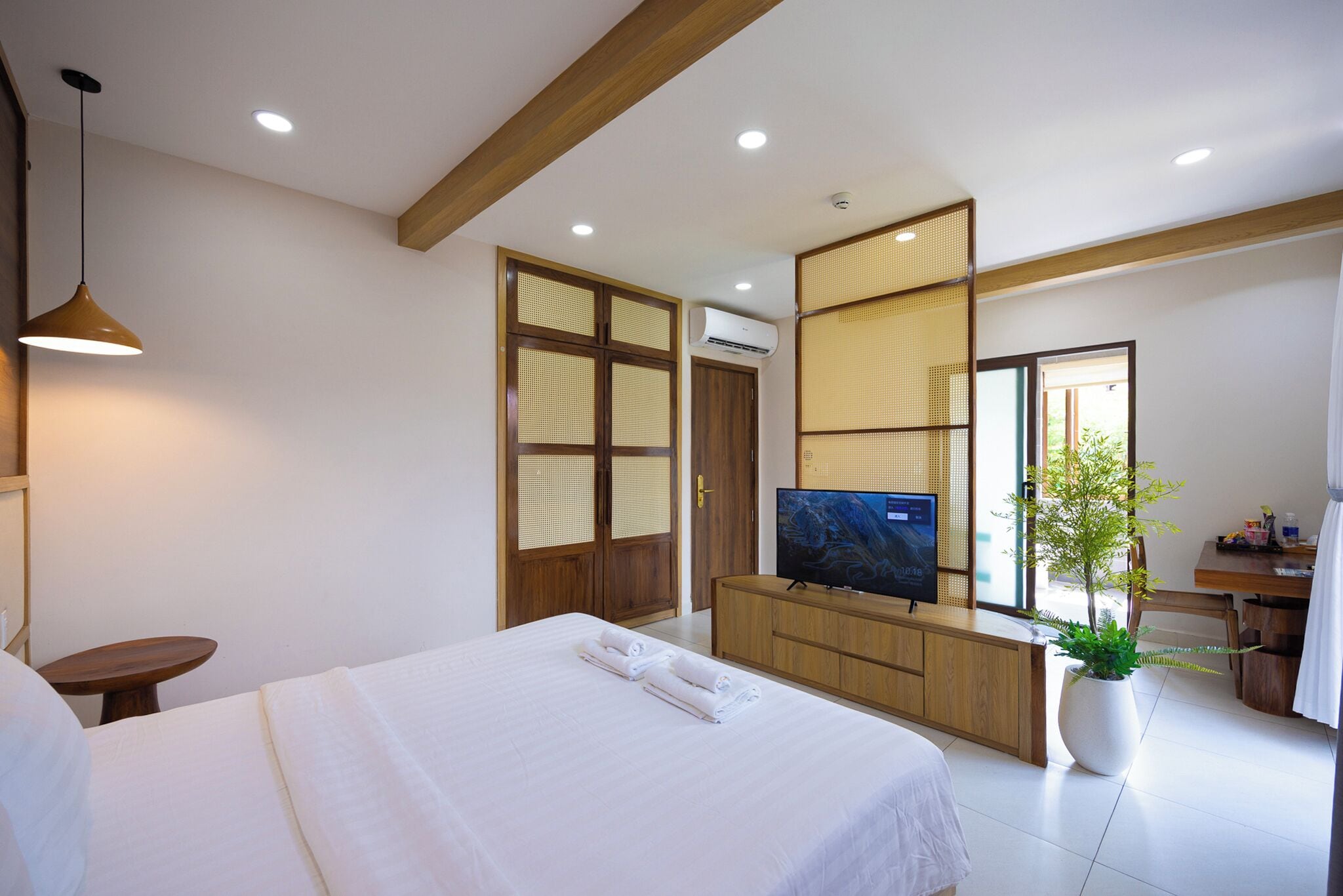 A hotel room with a bed, a TV, a potted plant, and a wooden cabinet.