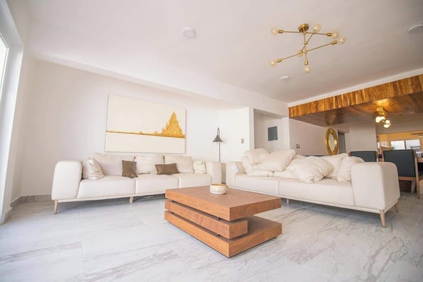 Un salon moderne avec un canapé blanc, une table basse en bois et un tableau représentant un paysage urbain accroché au mur.