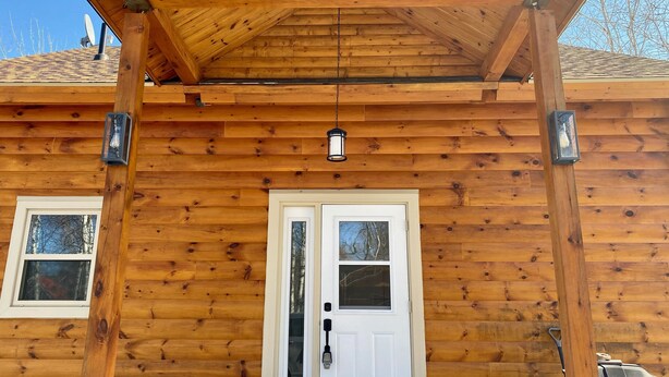 A wooden cabin with a covered porch, a white door, and two windows.