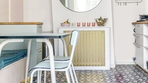 A compact room with a bed, a small table, a chair, a round mirror, and a patterned floor.