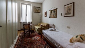 A bedroom with a single bed, a chair, a sofa, and a patterned rug. - Apartment in the historic center with private car parking (Mantova)