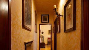 A hallway with patterned carpet, framed artwork on the walls, and a lit candle on a stand. - Apartment in the historic center with private car parking (Mantova)