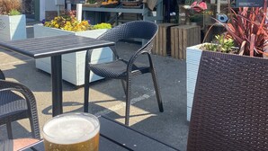 Et udendørs siddeområde med borde og stole foran en delikatessine og landbrugsbutik.