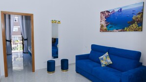 A room with a blue sofa, a painting of a coastal scene, a mirror, and a view of a balcony. - Natalia House center of Sorrento (Sorrento)
