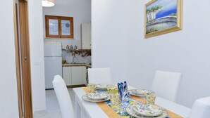 A dining area with a table set for four, white chairs, and a painting on the wall. - Natalia House center of Sorrento (Sorrento)