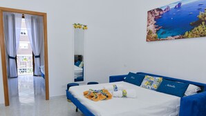 A bedroom with a bed, a blue sofa, and a painting of a coastal scene. - Natalia House center of Sorrento (Sorrento)