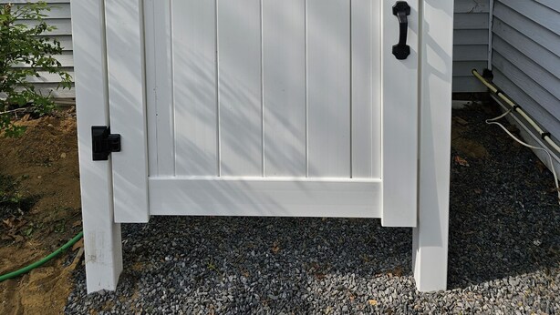 A white wooden gate with black hardware, attached to a house with white siding and green shutters. - Newly Renovated Mid-Cape Home with Pond and Waterfront Access (Dennis)