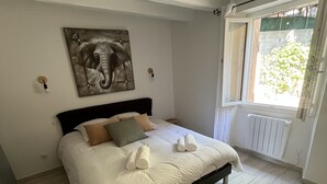 Een slaapkamer met een bed, een olifant schilderij, een raam en een radiator.