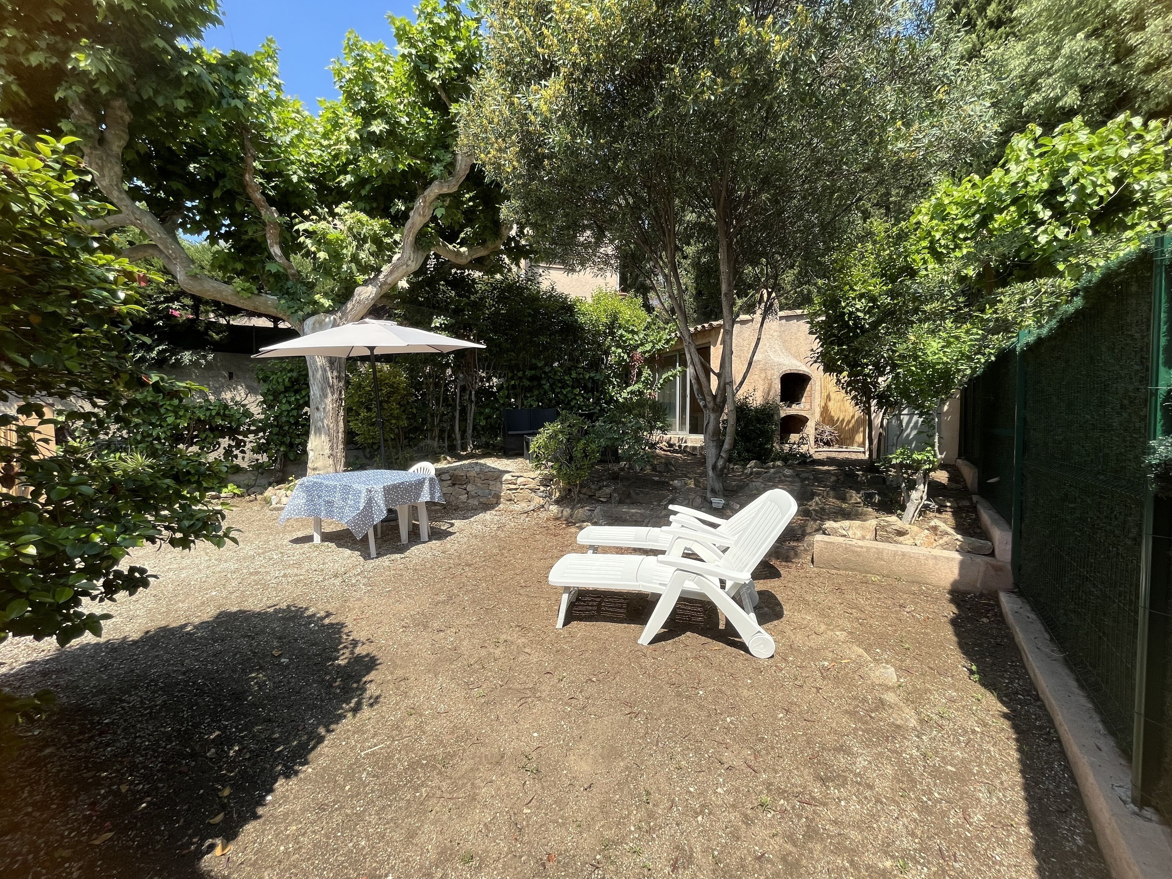 Un patio con mesa y sillas, rodeado de árboles y un muro de piedra.
