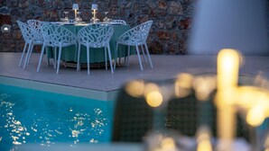 Un espace de restauration en plein air avec un mur en pierre en arrière-plan, une piscine et des chaises blanches.