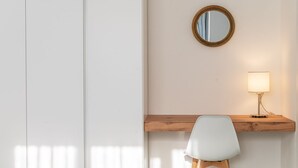 Ein Schlafzimmer mit einem Bett, einem Nachttisch mit Lampe, einem Sessel und einem Spiegel an der Wand.