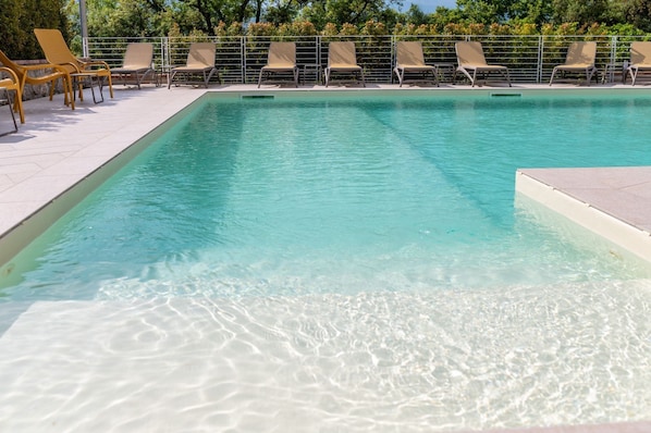 A clear swimming pool with lounge chairs and a tiled deck.