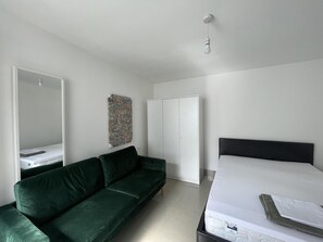 A modern bedroom with a green sofa, a bed with a white mattress, a wardrobe, and a ceiling light. - Immaculate 1-bed Studio in London (London)