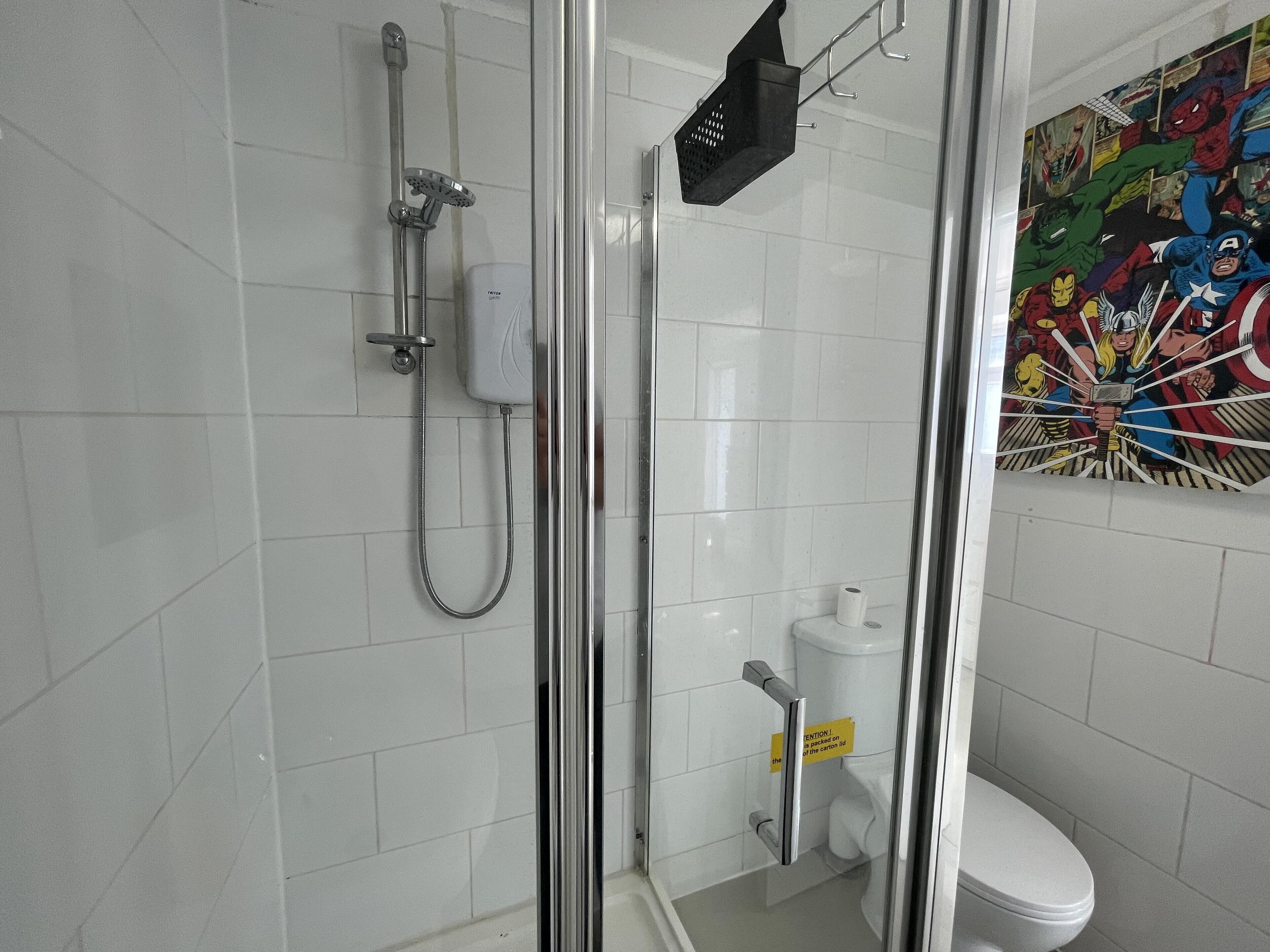 A bathroom with a shower, toilet, and a wall with a superhero-themed mural.