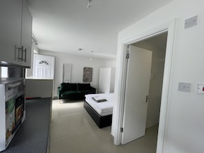 A modern bedroom with a bed, a green sofa, and a kitchen area with a microwave. - Immaculate 1-bed Studio in London (London)