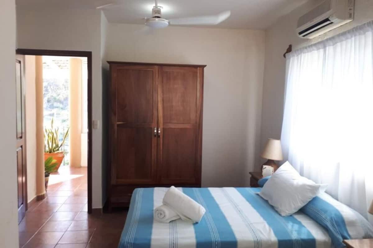 A bedroom with a bed, a wardrobe, a ceiling fan, an air conditioner, and a window with curtains.