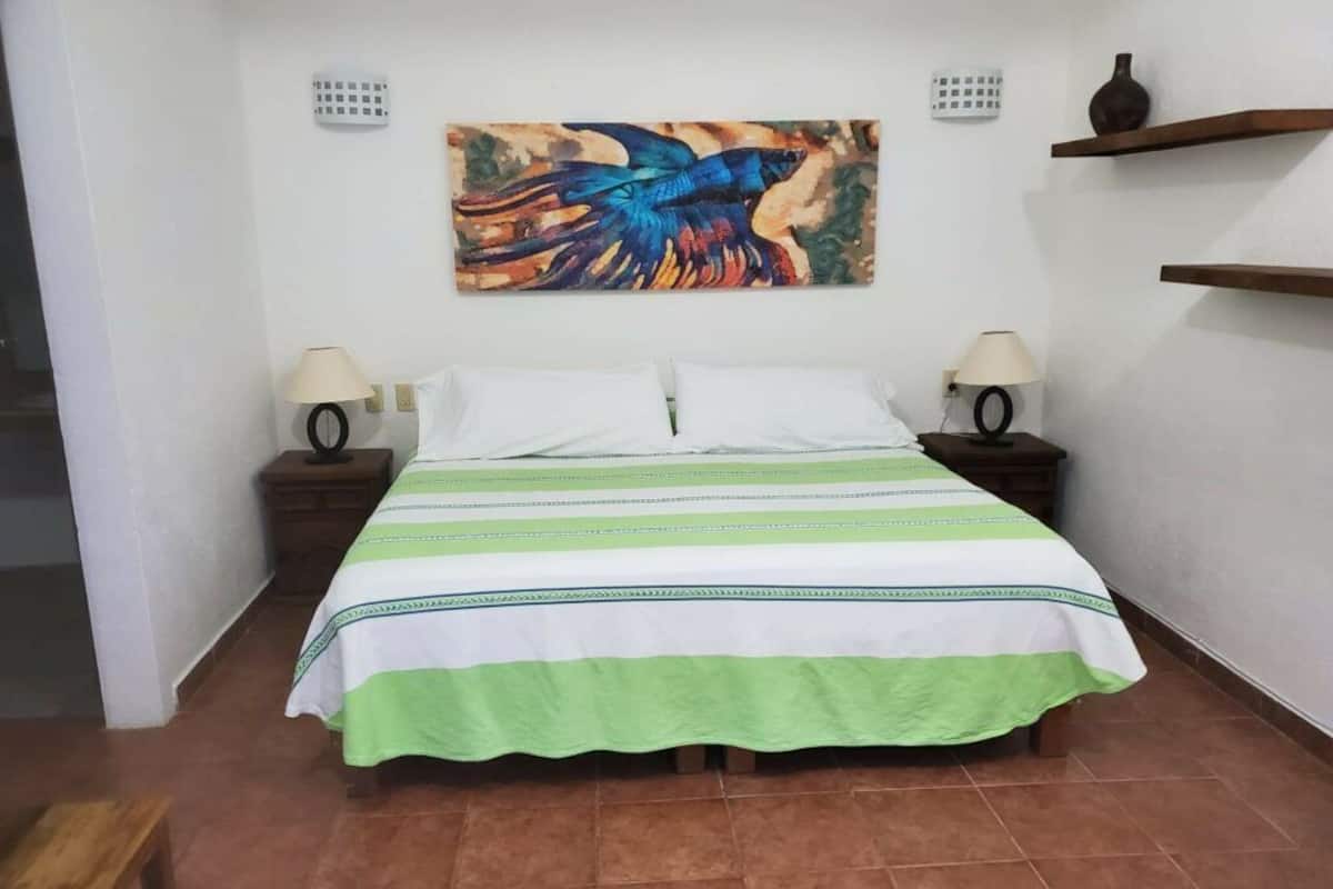 A hotel room with a bed, two nightstands, a painting on the wall, and a shelf with a vase.
