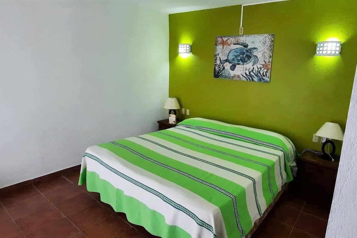 A room with a bed, two wall-mounted lights, a painting, and a tiled floor.
