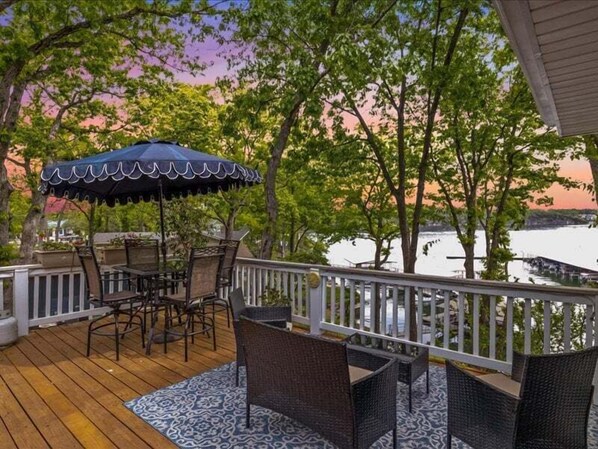 A wooden deck with outdoor furniture and a view of a body of water. - NEW! Lakefront Home -Amazing Dock -22mm -Sleeps 18 (Osage Beach)