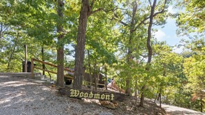 Un panneau en bois portant l’inscription « Woodmont », situé dans une zone boisée, avec des arbres et un chemin de gravier.