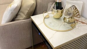 Una sala de estar moderna con un sofá color beige, una mesa de centro de vidrio con una bandeja dorada y una botella de champán.