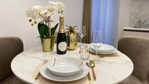 Mesa de comedor dispuesta con platos blancos, cubiertos dorados y una botella de champán. Hay dos jarrones dorados con flores y un florero con forma de piña.