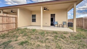 A covered patio area with two ceiling fans, a wooden fence, and a grassy lawn. - Home away from home (Seguin)