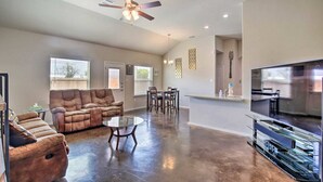 A spacious living room with a brown leather sofa, a glass coffee table, and a ceiling fan. There is a dining area with a table and chairs, and a kitchen area with a large TV and stainless steel appliances. - Home away from home (Seguin)