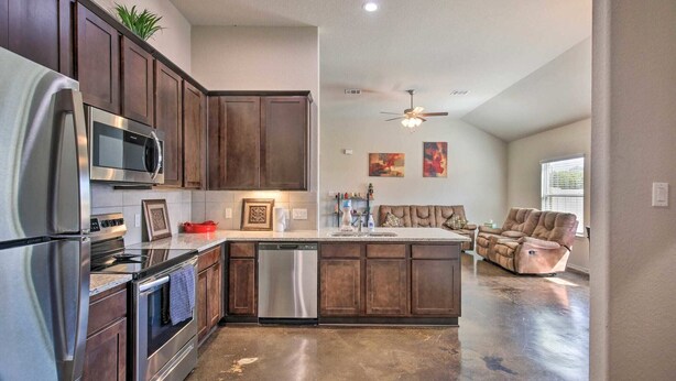 A modern kitchen with stainless steel appliances, dark wood cabinets, and a central island. - Home away from home (Seguin)
