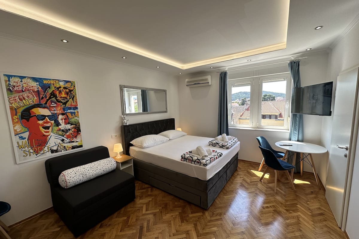 A modern hotel room with a large bed, a sofa, a small table, and a TV.