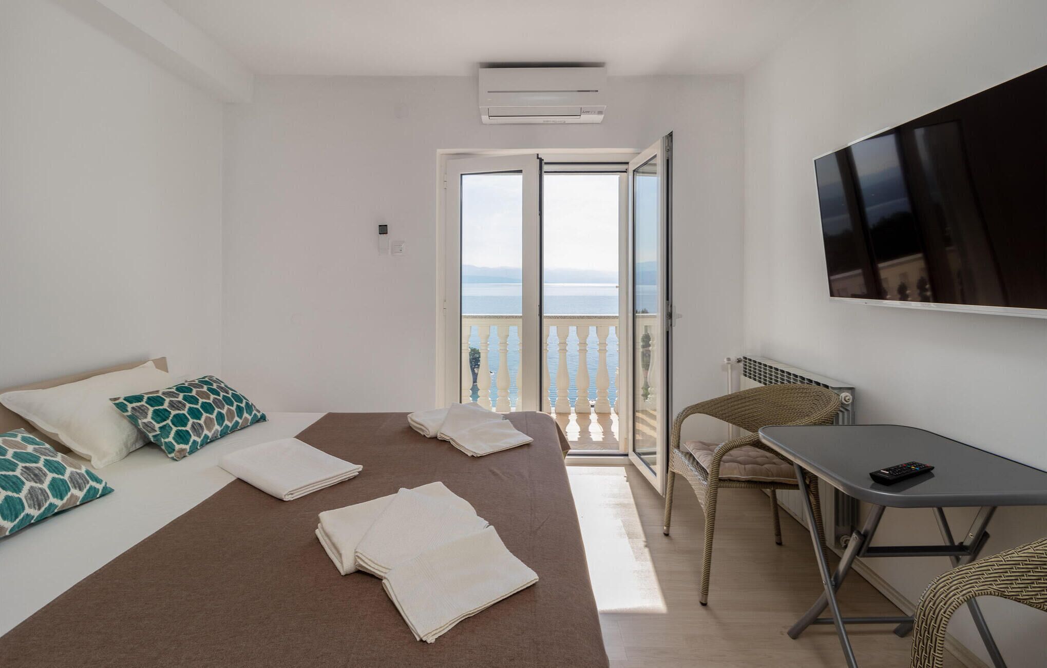 A bedroom with a bed, a TV, a table, and a view of the sea.